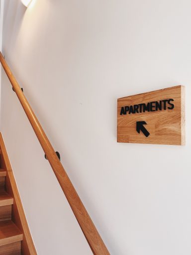 Holzschild mit der Aufschrift "Apartments" und Pfeil nach links an einer Treppe.